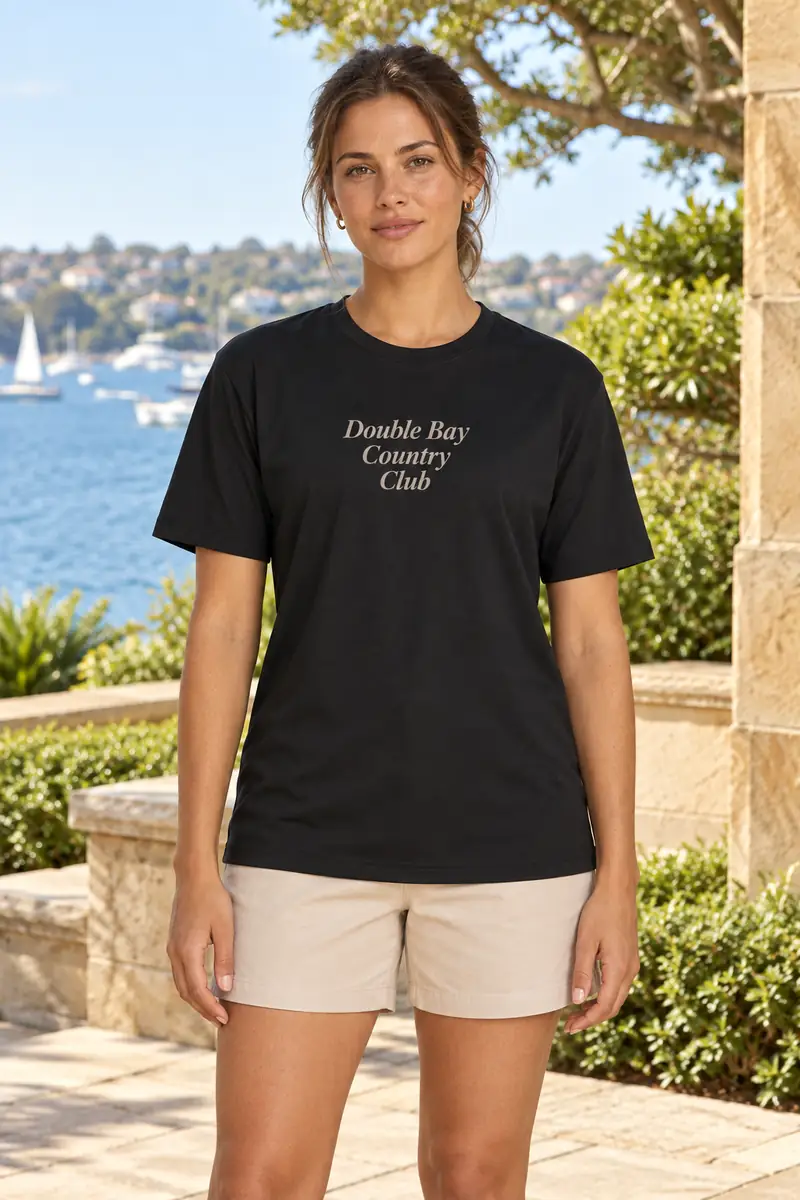 Concept imagery: a model wearing a black Double Bay Country Club tee, Sydney Harbour in the background — typography and fit not final
