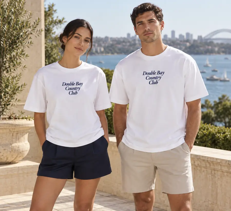 Concept imagery: two models wearing a white Double Bay Country Club tee, Sydney Harbour in the background — typography and fit not final